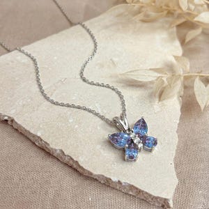 May include: A silver butterfly pendant necklace with blue and white gemstones. The butterfly design features a cluster of blue teardrop-shaped stones and small white stones. The necklace chain is delicate and silver.