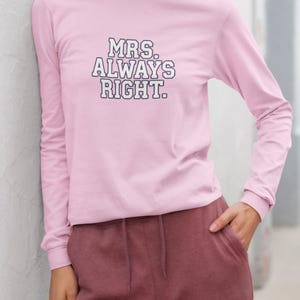 May include: A light pink long-sleeve shirt with the text "MRS. ALWAYS RIGHT" in a bold, black and white font. The shirt is paired with maroon sweatpants. The outfit is casual and comfortable.