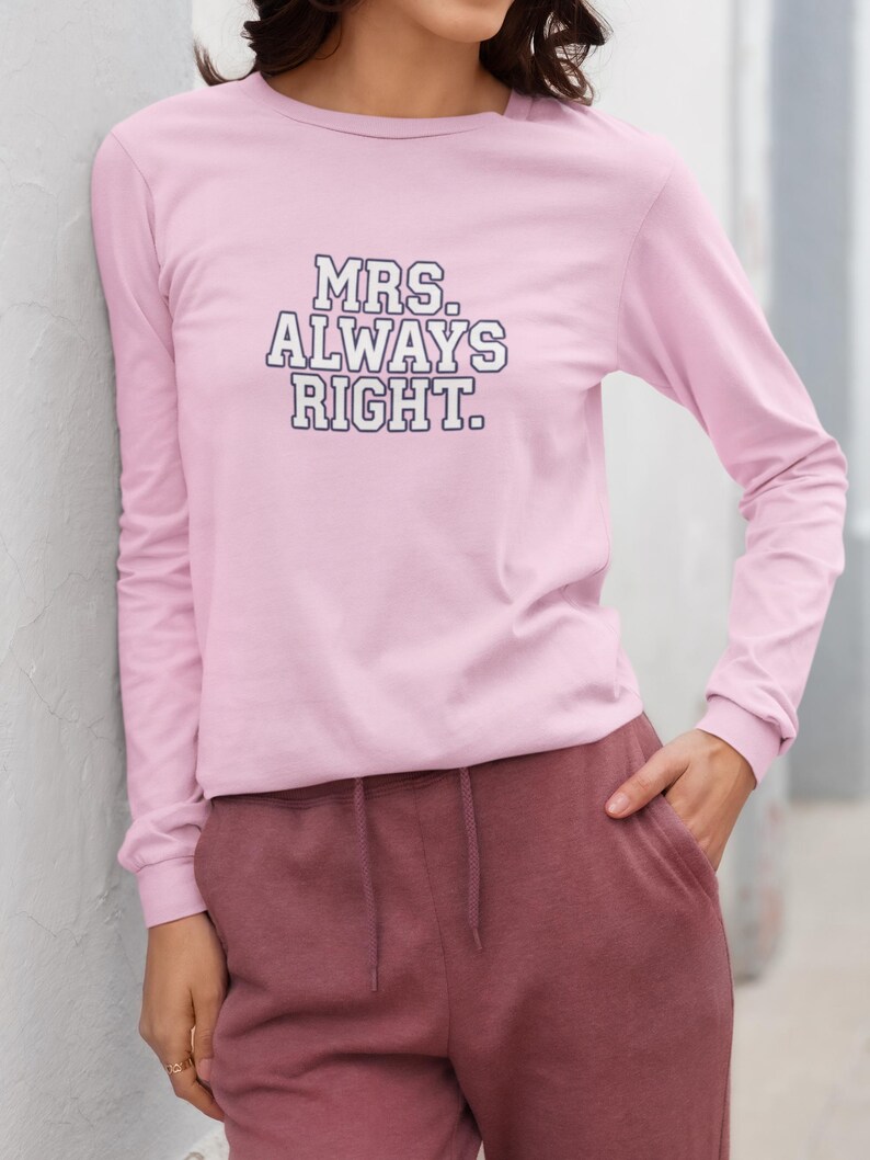 May include: A light pink long-sleeve shirt with the text "MRS. ALWAYS RIGHT" in a bold, black and white font. The shirt is paired with maroon sweatpants. The outfit is casual and comfortable.