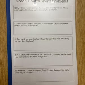 May include: A white sheet of paper titled Grade 1 Math Word Problems inside a clear plastic sleeve with a blue spine. The document contains five numbered maths problems involving apples, cookies, toy cars, crayons, and birds with empty boxes.