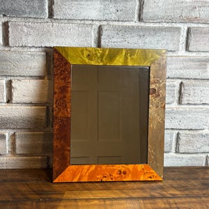 May include: A rectangular mirror featuring a frame constructed from four distinct segments of wood veneer. Each side of the frame displays a unique burl wood grain pattern with varying shades of brown, tan, and golden yellow, creating a multi-toned appearance.