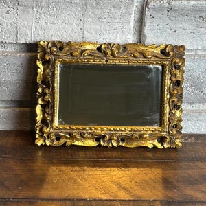 May include: A rectangular mirror featuring an ornate, distressed gold-tone frame with intricate carved scrollwork and leaf-like patterns. The mirror glass is set within a beaded inner border, creating a textured appearance throughout the frame.