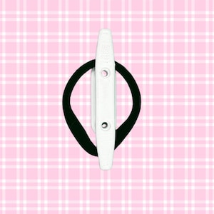 May include: A white hair clip with two holes and a black elastic band, set against a pink plaid background. The clip is rectangular with a rounded top and is designed to hold hair in place.