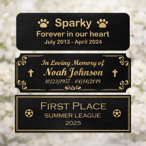 May include: Three rectangular black metal plaques with gold engraved text. The top plaque reads Sparky, Forever in our heart, July 2013 - April 2024 with paw prints. The middle reads In Loving Memory of Noah Johnson, 10/23/1957 - 04/14/2019 with crosses. The bottom reads FIRST PLACE, SUMMER LEAGUE, 2025 with soccer balls.