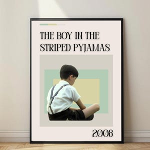 May include: Framed poster featuring the text "THE BOY IN THE STRIPED PYJAMAS" above an image of a young boy in a white shirt and suspenders. The year "2008" is printed at the bottom. The background has pastel green and yellow rectangles.