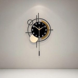 May include: A modern wall clock with a black face, gold accents, and a minimalist design. The clock features black hands, a gold-colored partial ring, and a pendulum. The clock is mounted on a light gray wall.