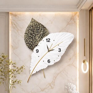 May include: A decorative wall clock in the shape of two overlapping leaves. One leaf is white with a clock face, the other is black with gold dot detailing. The clock hands and stems are gold.