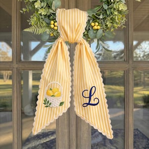 May include: A yellow and white striped fabric door hanger with scalloped lace edges. One side features an embroidered basket of yellow lemons with green leaves, and the other side displays a large, dark blue embroidered cursive letter L.