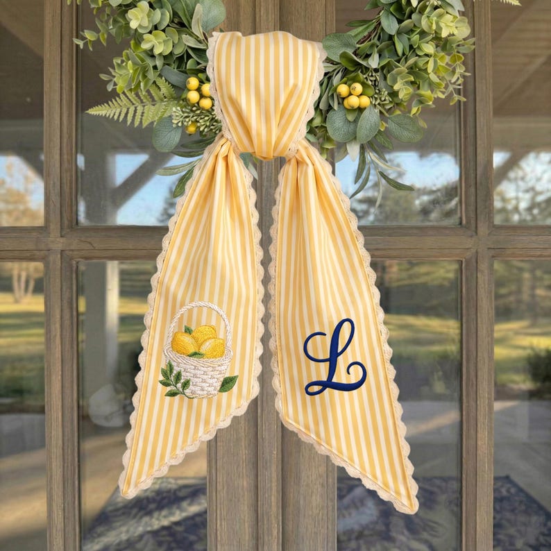 May include: A yellow and white striped fabric door hanger with scalloped lace edges. One side features an embroidered basket of yellow lemons with green leaves, and the other side displays a large, dark blue embroidered cursive letter L.