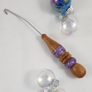 May include: A wooden crochet hook with a purple and white patterned handle and a silver metal hook.
