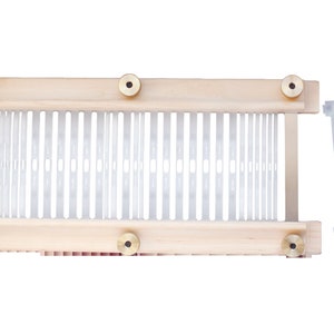 May include: A wooden loom with white plastic weaving needles and four brass knobs. The loom is accompanied by six white plastic weaving heddles.