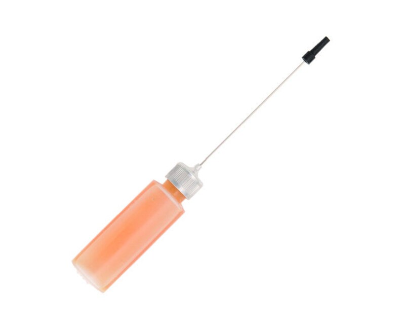 May include: A clear plastic bottle filled with an orange liquid, featuring a silver cap and a long, thin metal applicator with a black tip. The bottle is angled diagonally against a white background.