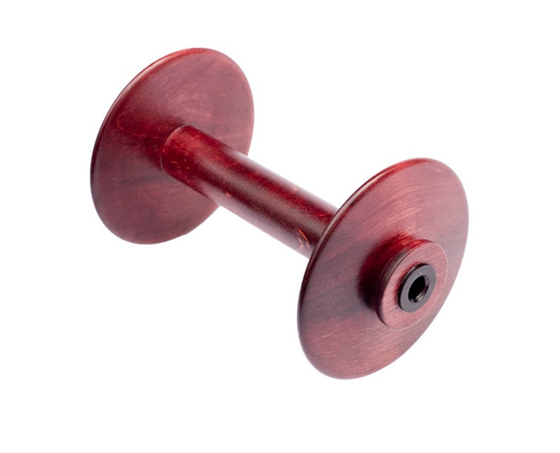 May include: A wooden dumbbell-shaped object with a deep red stain. The dumbbell has two circular ends connected by a cylindrical handle. The ends have a slightly raised center with a black insert. The wood grain is visible.