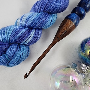 May include: A wooden crochet hook with a blue and white marbled handle. The hook is 4 mm and is next to a skein of blue and white yarn.