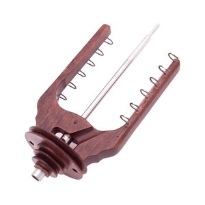 May include: A wooden yarn swift with a dark brown finish. The swift has a central metal rod and multiple metal loops along the arms. The base features a tiered design. The swift is designed to hold yarn for knitting or crocheting.