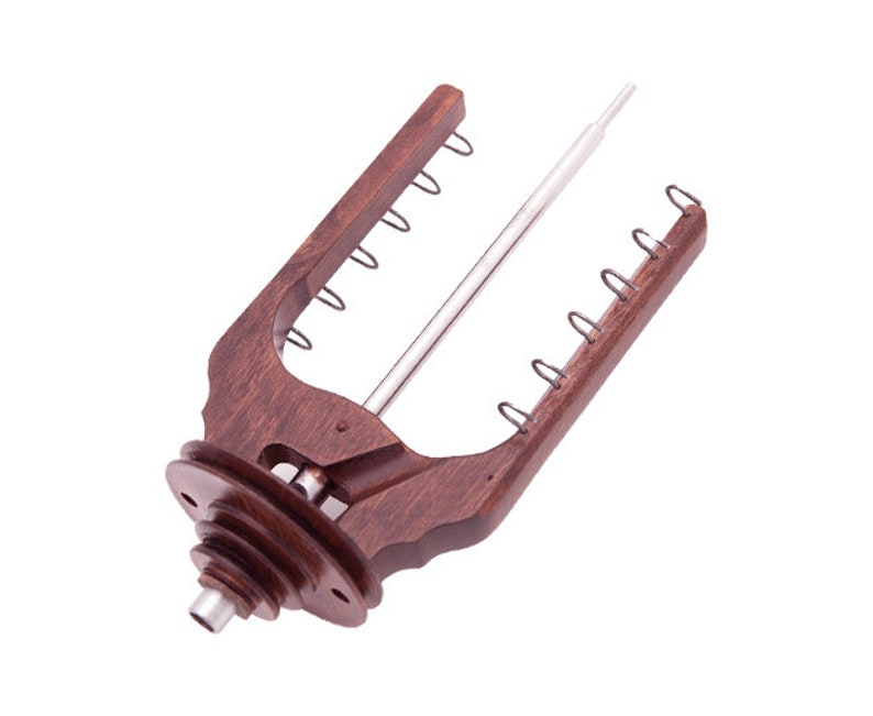 May include: A wooden yarn swift with a dark brown finish. The swift has a central metal rod and multiple metal loops along the arms. The base features a tiered design. The swift is designed to hold yarn for knitting or crocheting.