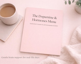 May include: A pink book titled "The Dopamine & Hormones Menu" with text about brain health, next to a mug of coffee on a light-colored surface. A small plant and a folded blanket are also in the image.