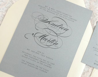 May include: A gray wedding invitation with a white envelope. The invitation features a calligraphic design with the names "Andica Monella" and "Martin Kole" and the wedding date and location. The text reads "Mr. & Mrs. Jason Frampton request the pleasure of your company at the wedding of their daughter Andica Monella to Martin Kole, Son of Mr. and Mrs. Kole Rubach, Saturday, the fifth day of June two thousand twenty-one, seven o'clock in the evening, The Treasury on the Plaza, Saint Augustine, Florida."