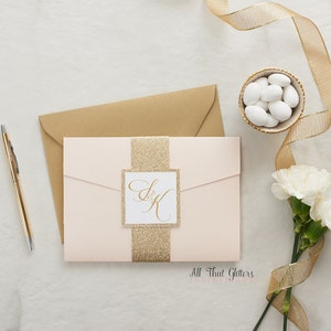 May include: A blush pink wedding invitation with a gold glitter band and a square card with the initials "S & K" in gold calligraphy. The text "All That Glitters" is printed at the bottom of the invitation.
