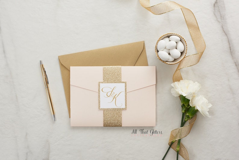 May include: A blush pink wedding invitation with a gold glitter band and a square card with the initials "S & K" in gold calligraphy. The text "All That Glitters" is printed at the bottom of the invitation.