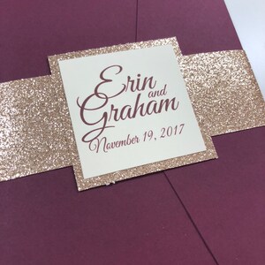 May include: Burgundy wedding invitation with a gold glitter band and a cream card with the text "Erin and Graham, November 19, 2017".