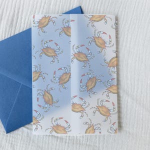 May include: A blue envelope next to a folded card with a crab pattern. The card features repeating illustrations of crabs in shades of orange, white, and red on a light blue background. The envelope is a solid, deep blue color.