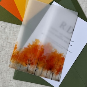 May include: An invitation suite featuring a translucent overlay with an autumn tree design in shades of orange and red. The suite includes a white card and is set in a green envelope, with additional orange and yellow paper accents.