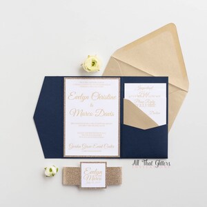 May include: Navy blue wedding invitation with a gold glitter border and gold lettering. The invitation reads "Evelyn Christine & Marco Davis". The invitation is accompanied by a smaller card with the text "Suggested Hotel" and a gold glitter ribbon with the text "Evelyn & Marco" on it.