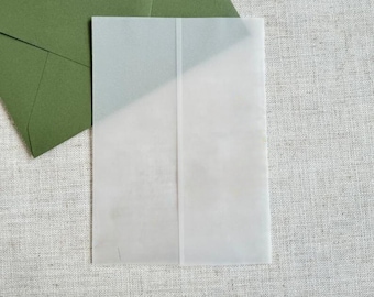 May include: A white envelope with a crease down the center. The envelope is lying on a textured, light brown surface.