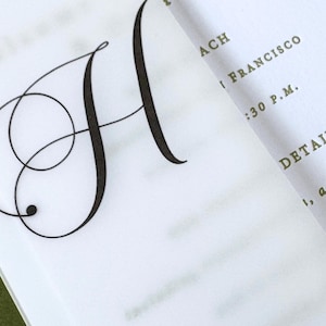Puede incluir: Primer plano de una invitaci&oacute;n blanca con una gran y elegante letra negra "H" en fuente cursiva. La invitaci&oacute;n tambi&eacute;n incluye detalles en fuente verde, como "ACH", "I FRANCISCO" y "DETAILS".