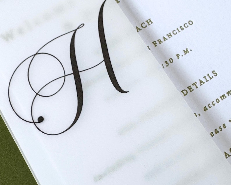 Puede incluir: Primer plano de una invitaci&oacute;n blanca con una gran y elegante letra negra "H" en fuente cursiva. La invitaci&oacute;n tambi&eacute;n incluye detalles en fuente verde, como "ACH", "I FRANCISCO" y "DETAILS".