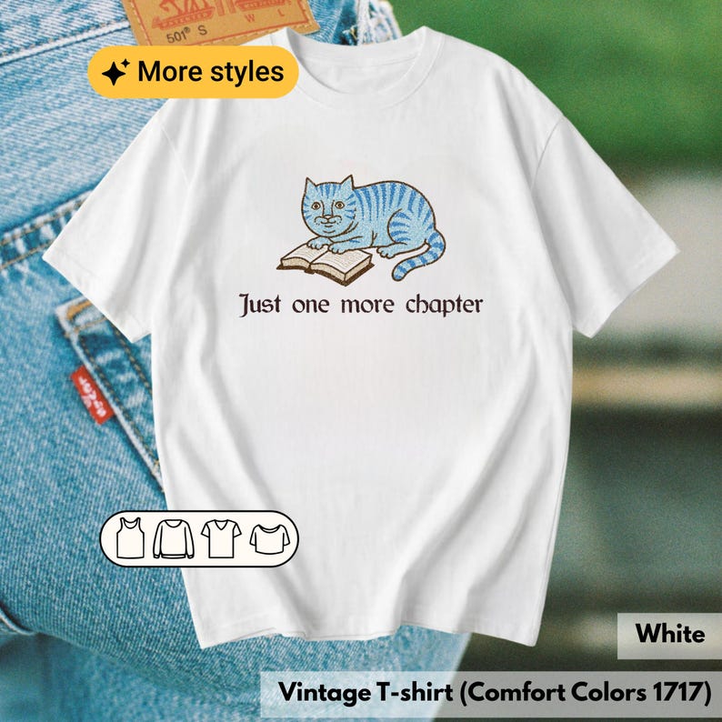 K&ouml;nnte beinhalten: Ein wei&szlig;es T-Shirt mit kurzen &Auml;rmeln und einer Grafik einer blau gestreiften Katze, die liegt und ein offenes Buch liest. Unter der Katze steht der Text "Just one more chapter" in einer dunklen Schrift. Das Shirt hat einen Rundhalsausschnitt.