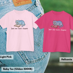K&ouml;nnte beinhalten: Zwei kurz&auml;rmelige T-Shirts, eines in Hellrosa und eines in Heliconia-Pink, jeweils mit einer Grafik einer blau gestreiften Katze, die auf einem offenen Buch liegt, und dem Text Just one more chapter in Schwarz unter dem Motiv auf dem hellrosa Shirt.