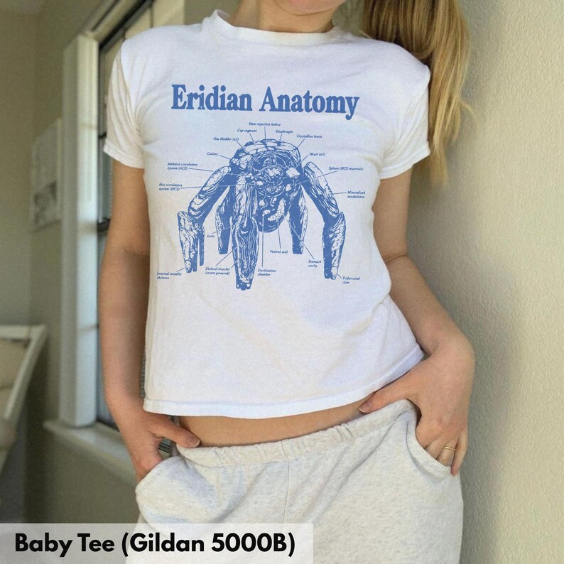 May include: A white short-sleeve t-shirt featuring a blue graphic print titled Eridian Anatomy. The design displays a detailed scientific illustration of a creature with multiple limbs, accompanied by various labels pointing to specific body parts.
