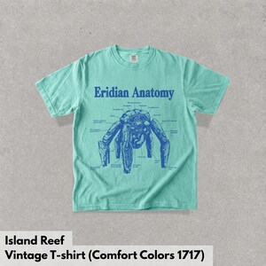 May include: A mint green short-sleeve t-shirt featuring a dark blue graphic print on the chest. The design displays a creature labeled Eridian Anatomy with various anatomical parts identified by thin lines and text in a scientific diagram style.