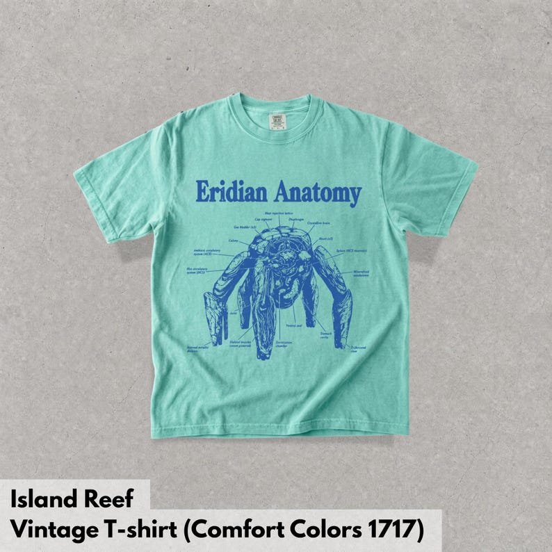 May include: A mint green short-sleeve t-shirt featuring a dark blue graphic print on the chest. The design displays a creature labeled Eridian Anatomy with various anatomical parts identified by thin lines and text in a scientific diagram style.