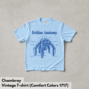 May include: A light blue short-sleeve t-shirt featuring a dark blue graphic print on the chest. The design displays a creature labeled Eridian Anatomy with various anatomical lines and text pointing to different parts of the creature's body.