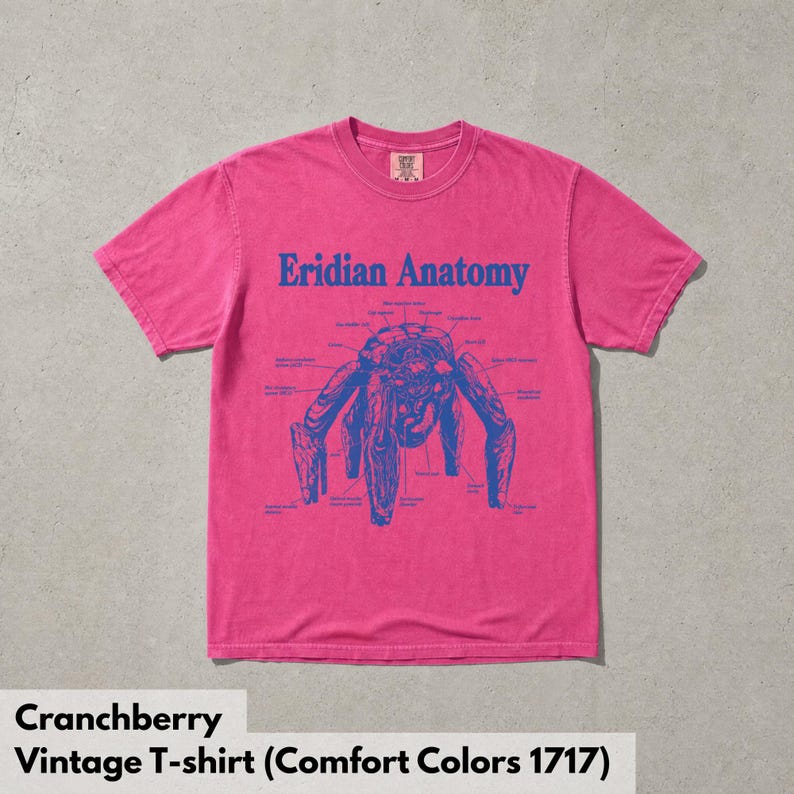 May include: A bright pink short-sleeve t-shirt featuring a blue graphic print on the chest. The design displays a complex creature illustration labeled Eridian Anatomy with various small text annotations pointing to specific parts of the figure.
