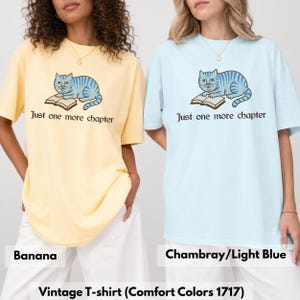 K&ouml;nnte beinhalten: Zwei kurz&auml;rmelige T-Shirts in Bananengelb und Chambray-Hellblau. Jedes Shirt zeigt eine Grafik einer blau gestreiften Katze, die auf einem offenen Buch liegt, mit dem darunter in dunkler Schrift gedruckten Text Just one more chapter.