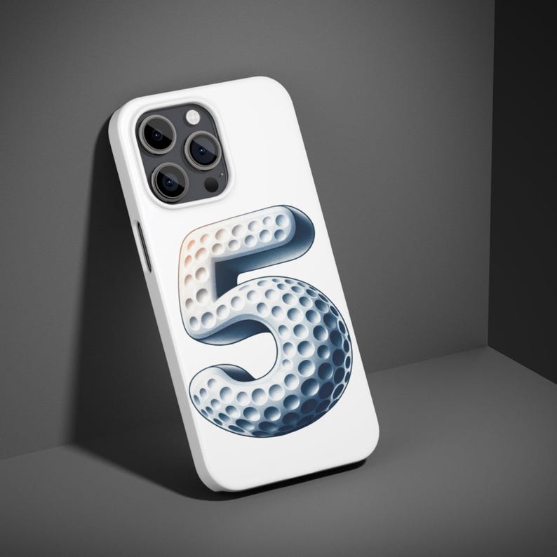 K&ouml;nnte beinhalten: Wei&szlig;es Handycase mit einem von einem Golfball inspirierten Design der Zahl 5. Die Zahl ist in Wei&szlig;- und Blaut&ouml;nen gehalten und hat eine strukturierte Oberfl&auml;che. Das Case hat eine gl&auml;nzende Oberfl&auml;che und mehrere Kameralinsen.