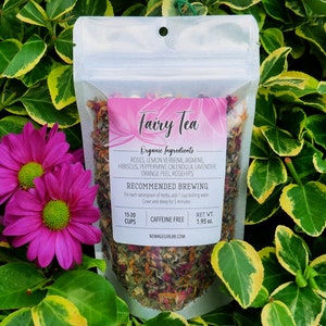 May include: A white resealable pouch filled with a blend of dried herbs and flowers for making tea. The label reads "Fairy Tea" and lists the ingredients: roses, lemon verbena, jasmine, hibiscus, peppermint, calendula, lavender, orange peel, and rosehips. The label also includes brewing instructions and states that the tea is caffeine free. The pouch contains 1.95 ounces of tea and is enough for 15-20 cups.