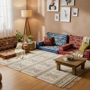 May include: A living room scene featuring low-profile floor seating in red and blue with intricate geometric patterns. A wooden coffee table and a patterned rug complete the cozy, bohemian-style space. Decorative pillows and a throw blanket add comfort.