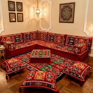 May include: A red sectional sofa with patterned cushions and a matching rug. The sofa is arranged in a corner, with decorative pillows and a low table. The room has a warm, inviting atmosphere.