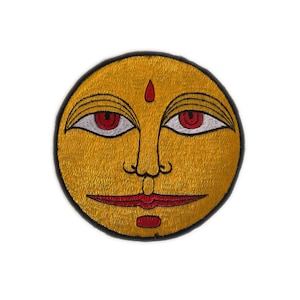 May include: Round embroidered patch depicting a sun face. The sun has a yellow background, red eyes and lips, and a small red dot on the forehead. Black outlines and a black border complete the design.