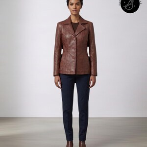 May include: A brown leather blazer with a notched collar, three front buttons, and vertical seam detailing, worn over a dark brown top and dark navy trousers, paired with brown leather ankle boots. A circular logo with the text FASHION INFLUENCER.