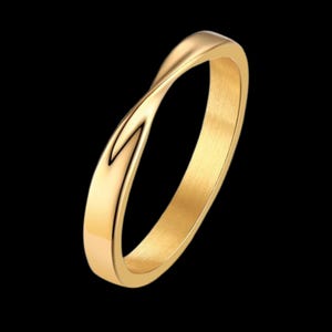 Puede incluir: Un anillo dorado con un diseño retorcido. El anillo tiene una superficie lisa y pulida y un estilo simple y elegante. El anillo está sobre un fondo negro.