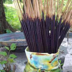 May include: A close-up of a bundle of dark brown incense sticks in a colorful ceramic vase. The sticks are arranged in a fan shape and are ready to be burned.