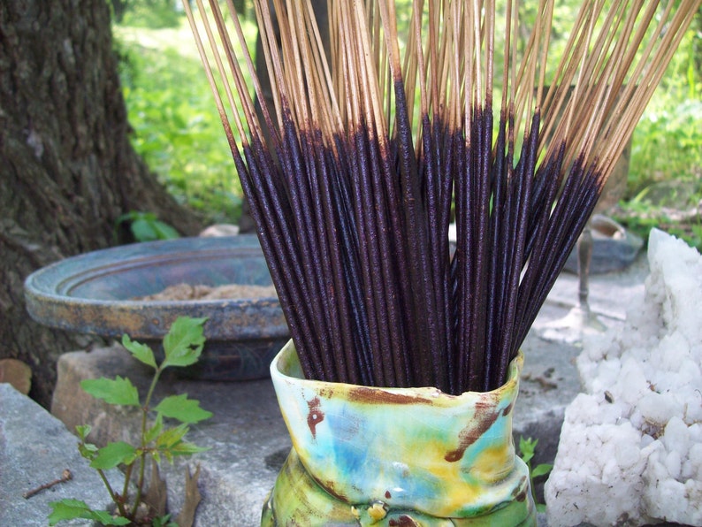 May include: A close-up of a bundle of dark brown incense sticks in a colorful ceramic vase. The sticks are arranged in a fan shape and are ready to be burned.
