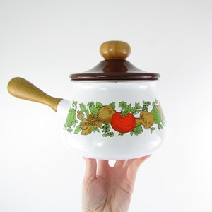 May include: White enamel saucepan with a brown lid and wooden handle. The saucepan features a colourful design of mushrooms, tomatoes, and greenery.