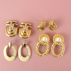May include: A set of six gold-tone earrings. Two pairs feature a geometric design with a white accent. One pair has a pearl-like accent. The other pair has a simple oval shape with a white enamel finish.
